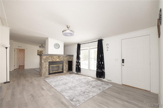 unfurnished living room with a stone fireplace, light hardwood / wood-style floors, and a textured ceiling