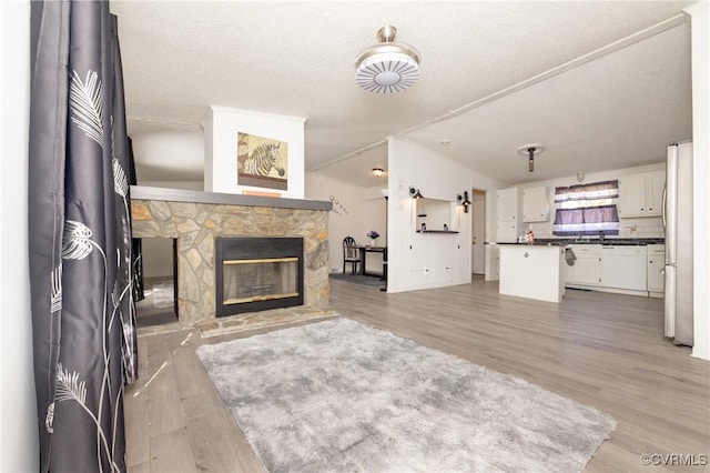 unfurnished living room with wood-type flooring, a textured ceiling, and a stone fireplace