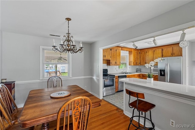 kitchen with appliances with stainless steel finishes, track lighting, sink, a chandelier, and light hardwood / wood-style floors