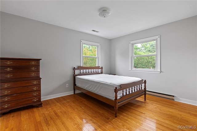 bedroom featuring light hardwood / wood-style flooring, multiple windows, and a baseboard heating unit