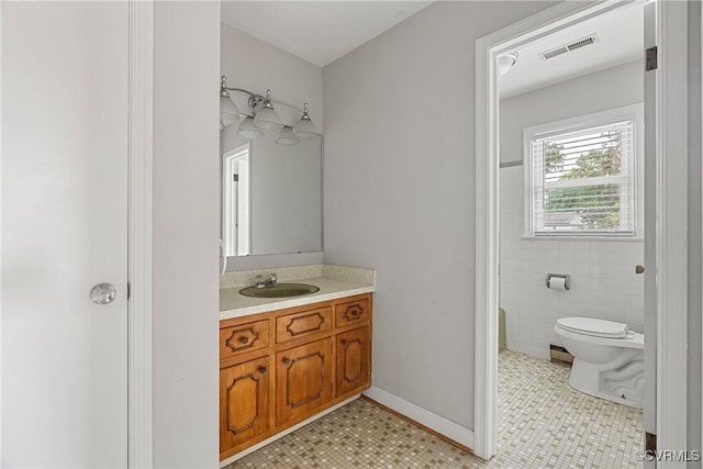 bathroom featuring toilet, vanity, tile patterned floors, and tile walls