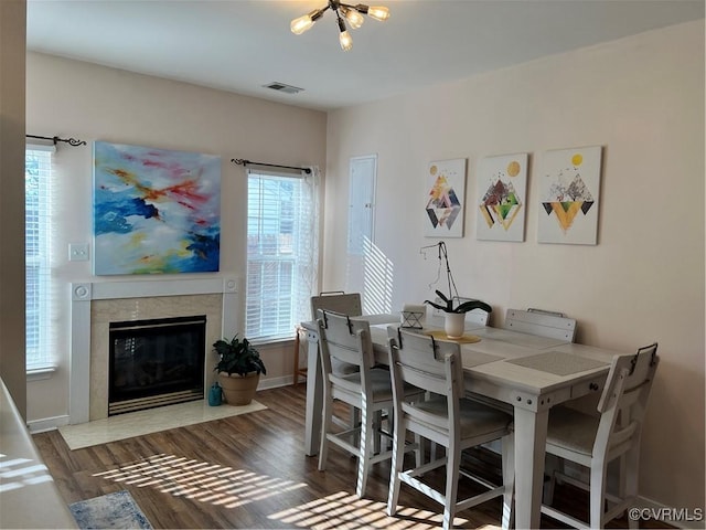 dining room featuring a tiled fireplace, dark hardwood / wood-style flooring, and an inviting chandelier