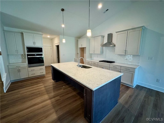 kitchen featuring stainless steel oven, sink, wall chimney range hood, vaulted ceiling, and a kitchen island with sink