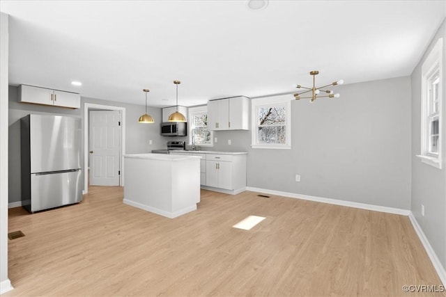 kitchen with white cabinetry, sink, hanging light fixtures, stainless steel appliances, and light wood-type flooring