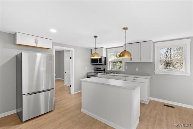 kitchen featuring sink, hanging light fixtures, stainless steel appliances, light hardwood / wood-style flooring, and white cabinets