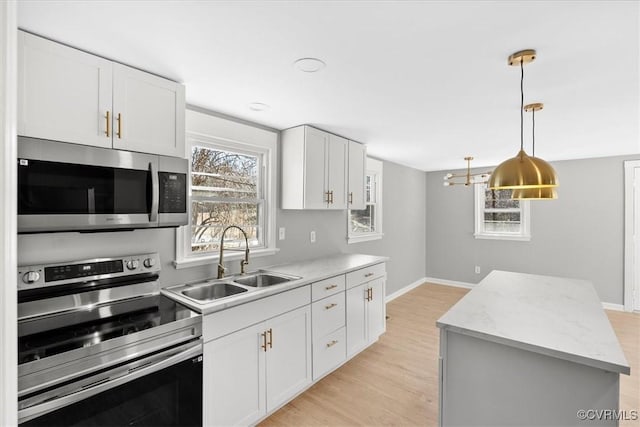 kitchen with white cabinets, hanging light fixtures, sink, appliances with stainless steel finishes, and a kitchen island