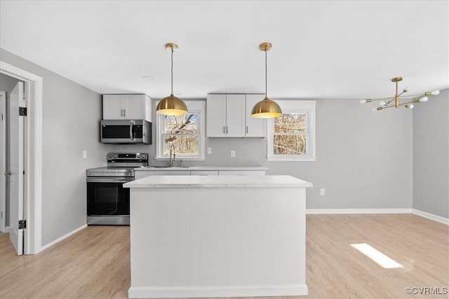 kitchen with light hardwood / wood-style flooring, white cabinets, stainless steel appliances, and decorative light fixtures