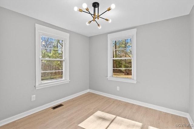 empty room featuring light hardwood / wood-style flooring, an inviting chandelier, and a wealth of natural light