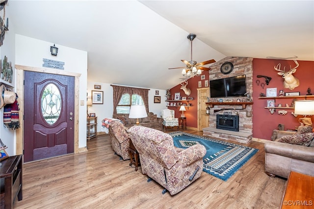 living room featuring a wood stove, ceiling fan, wood-type flooring, and vaulted ceiling