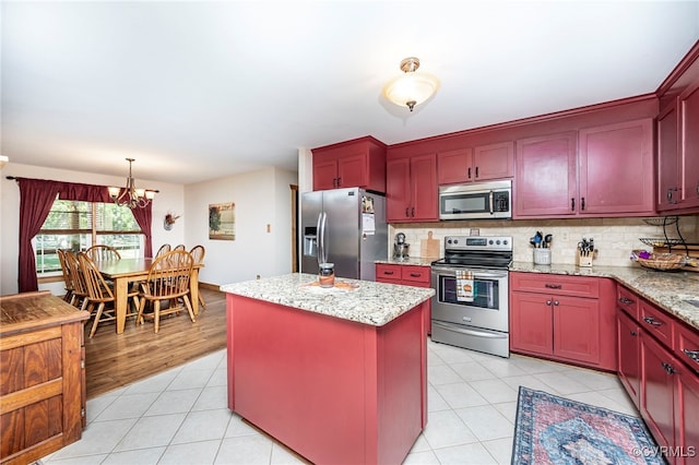 kitchen with decorative light fixtures, a kitchen island, light stone counters, stainless steel appliances, and a chandelier