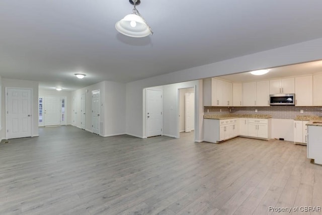 kitchen featuring tasteful backsplash, white cabinetry, hanging light fixtures, and light hardwood / wood-style floors