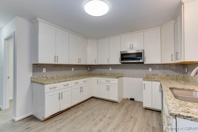 kitchen with sink, light hardwood / wood-style flooring, decorative backsplash, light stone counters, and white cabinetry