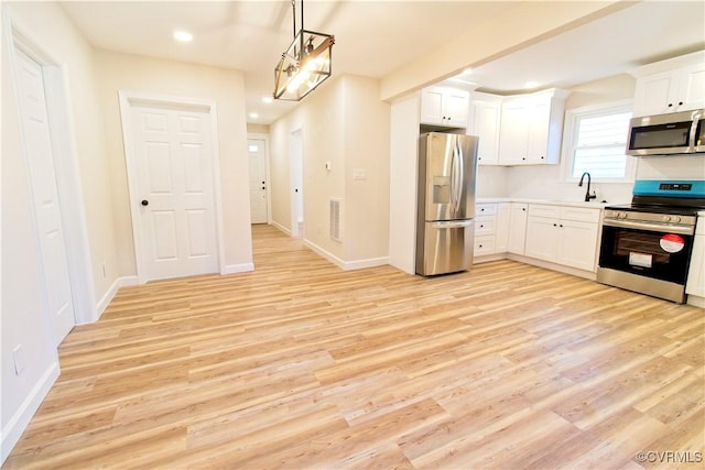 kitchen with white cabinetry, hanging light fixtures, stainless steel appliances, and light wood-type flooring