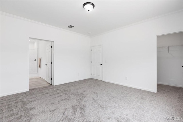 unfurnished bedroom with a walk in closet, light colored carpet, a closet, and crown molding