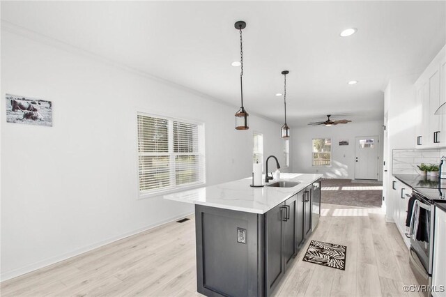 kitchen featuring electric range, ceiling fan, light stone counters, an island with sink, and pendant lighting