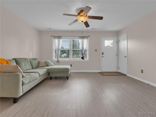 living room featuring a ceiling fan, baseboards, and light wood finished floors