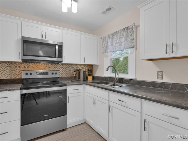 kitchen with visible vents, a sink, appliances with stainless steel finishes, white cabinetry, and dark countertops