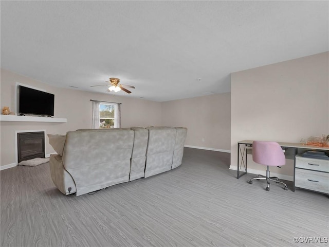 living room featuring a glass covered fireplace, baseboards, wood finished floors, and ceiling fan