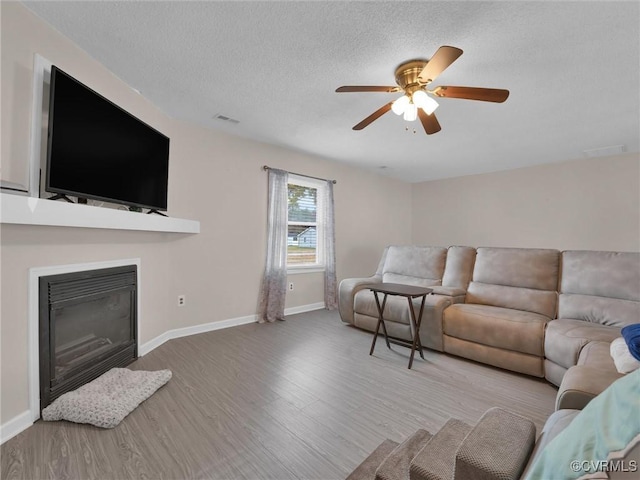 living area with visible vents, baseboards, wood finished floors, a glass covered fireplace, and a textured ceiling