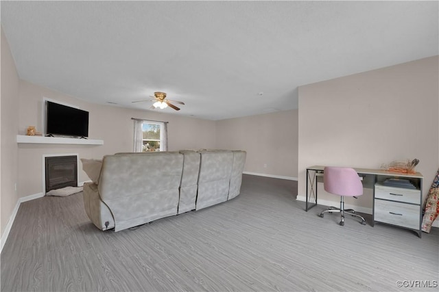 living room with a glass covered fireplace, wood finished floors, baseboards, and a ceiling fan