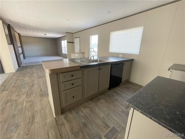 kitchen with dishwasher, sink, hardwood / wood-style floors, a textured ceiling, and a kitchen island with sink