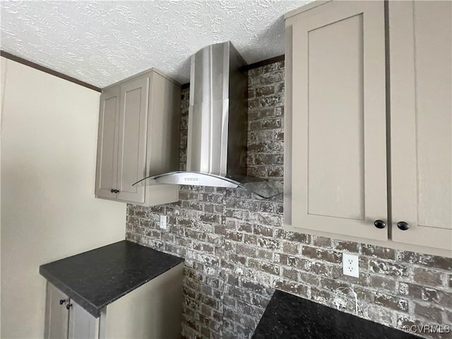 kitchen with gray cabinets, wall chimney range hood, a textured ceiling, and brick wall