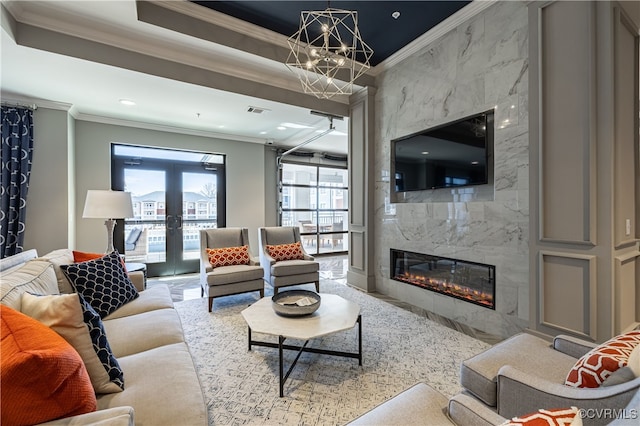 living room with ceiling fan with notable chandelier, crown molding, a high end fireplace, and french doors