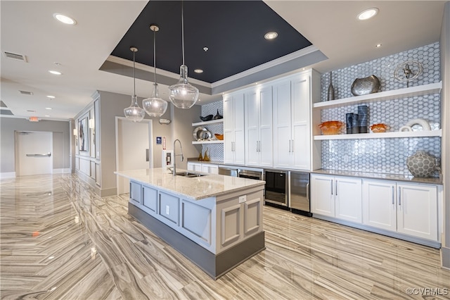 kitchen featuring a center island with sink, sink, decorative light fixtures, light stone counters, and white cabinetry