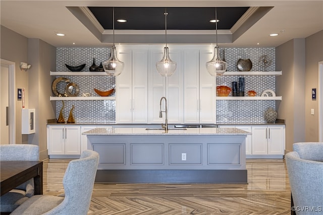 bar featuring a raised ceiling, hanging light fixtures, and sink