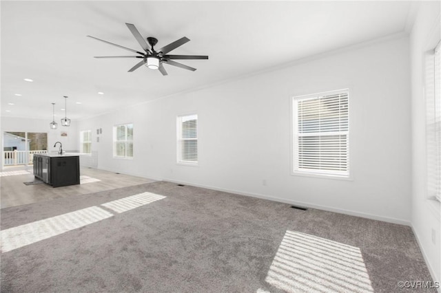 unfurnished living room with crown molding, sink, carpet, and ceiling fan