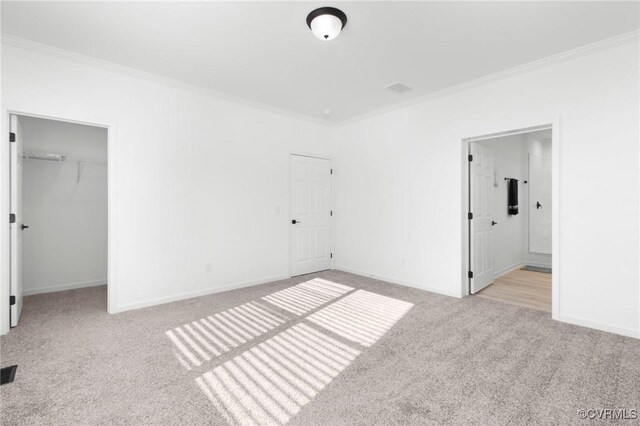 unfurnished bedroom featuring a closet, light carpet, crown molding, and a walk in closet