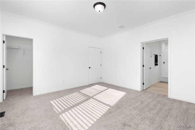 unfurnished bedroom with crown molding, light colored carpet, ensuite bath, and a walk in closet