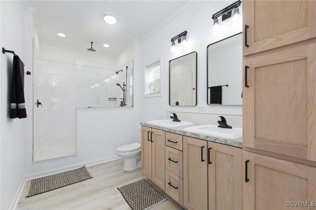 bathroom with vanity, crown molding, toilet, a tile shower, and wood-type flooring