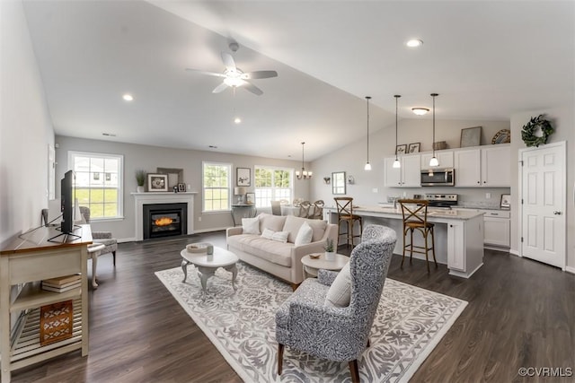 living room featuring lofted ceiling, dark wood-type flooring, and ceiling fan with notable chandelier