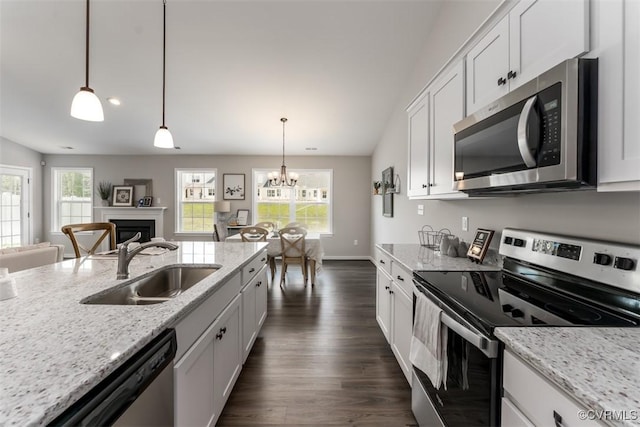 kitchen with light stone countertops, sink, white cabinetry, hanging light fixtures, and stainless steel appliances