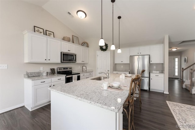 kitchen with appliances with stainless steel finishes, light stone counters, white cabinets, hanging light fixtures, and an island with sink