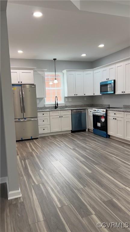 kitchen with sink, hanging light fixtures, stainless steel appliances, and light wood-type flooring