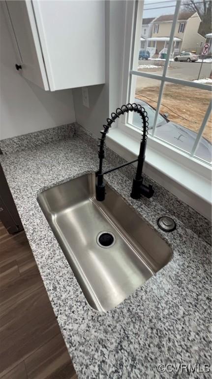 interior details featuring white cabinetry, sink, light stone countertops, and dark hardwood / wood-style floors