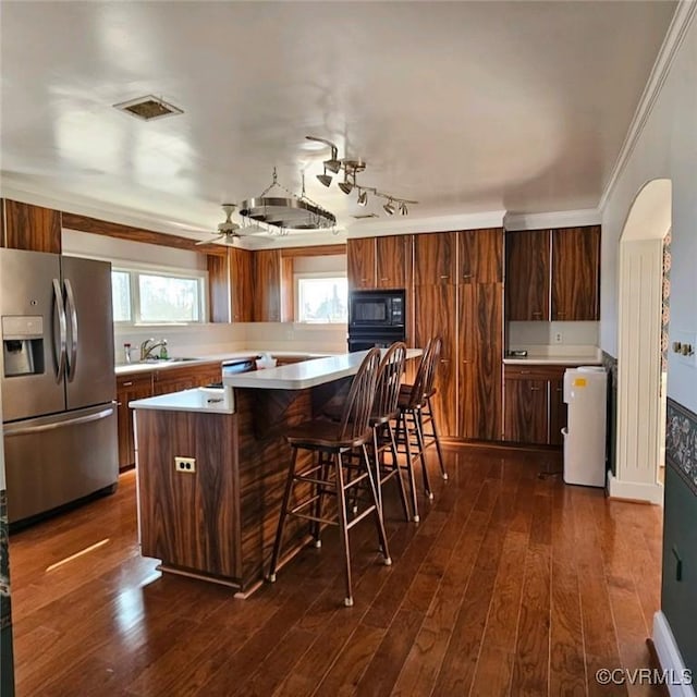 kitchen with stainless steel fridge, dark wood-type flooring, sink, a kitchen island, and a breakfast bar area