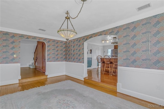 unfurnished room featuring arched walkways, a wainscoted wall, wallpapered walls, and visible vents