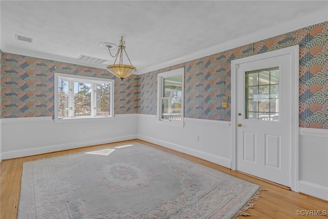 unfurnished dining area with wallpapered walls, wood finished floors, visible vents, and wainscoting