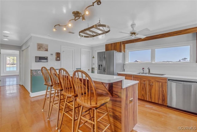 kitchen featuring a kitchen bar, light wood-style flooring, brown cabinets, stainless steel appliances, and a sink