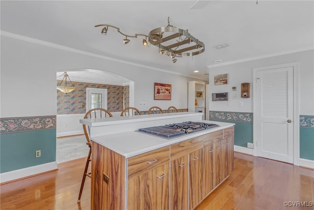 kitchen featuring wallpapered walls, stainless steel gas stovetop, wainscoting, crown molding, and a kitchen breakfast bar