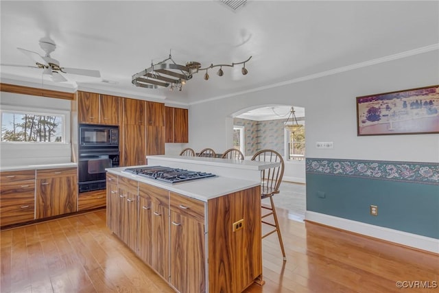 kitchen with a breakfast bar, black appliances, arched walkways, and brown cabinets