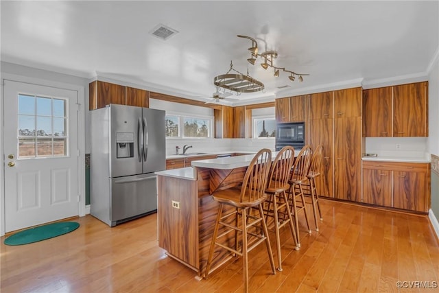 kitchen featuring visible vents, black microwave, stainless steel refrigerator with ice dispenser, brown cabinetry, and a sink