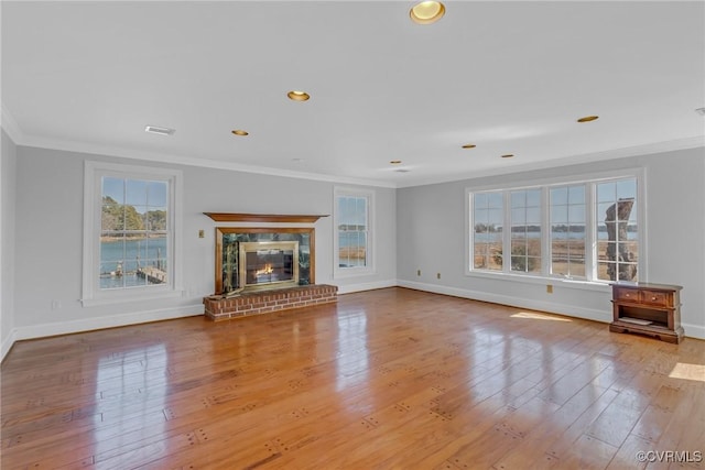 unfurnished living room featuring visible vents, ornamental molding, a glass covered fireplace, and wood-type flooring