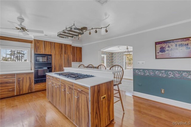 kitchen featuring black appliances, a breakfast bar area, brown cabinetry, and arched walkways