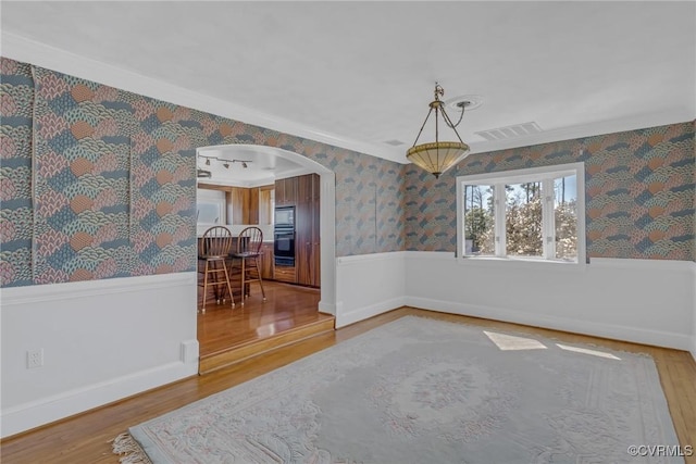 spare room with a wainscoted wall, visible vents, wood finished floors, arched walkways, and wallpapered walls