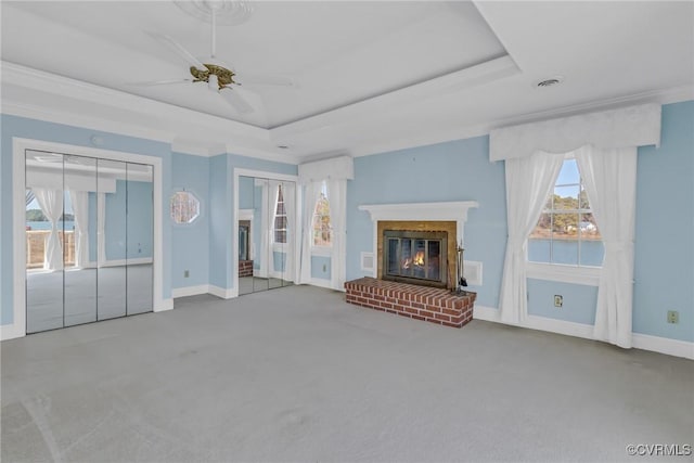 unfurnished living room with carpet, baseboards, a tray ceiling, ceiling fan, and a brick fireplace