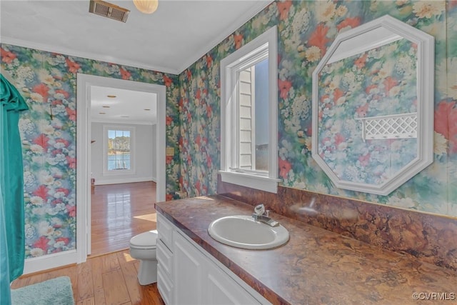 bathroom featuring visible vents, toilet, wood finished floors, wallpapered walls, and vanity